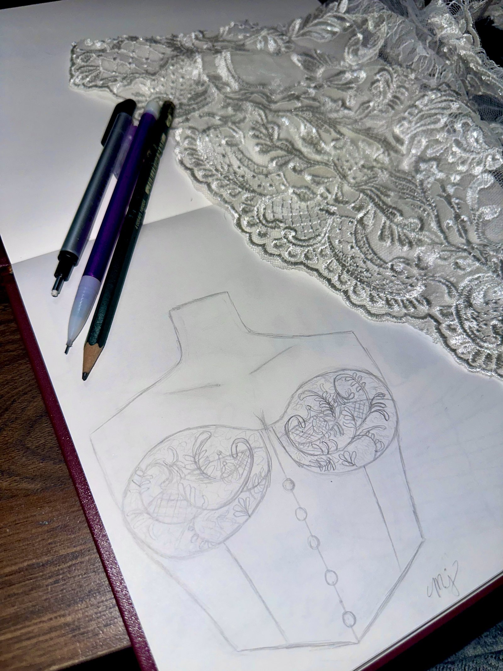 A sketch and a length of beaded lace beside designer's pencils on a workbench
