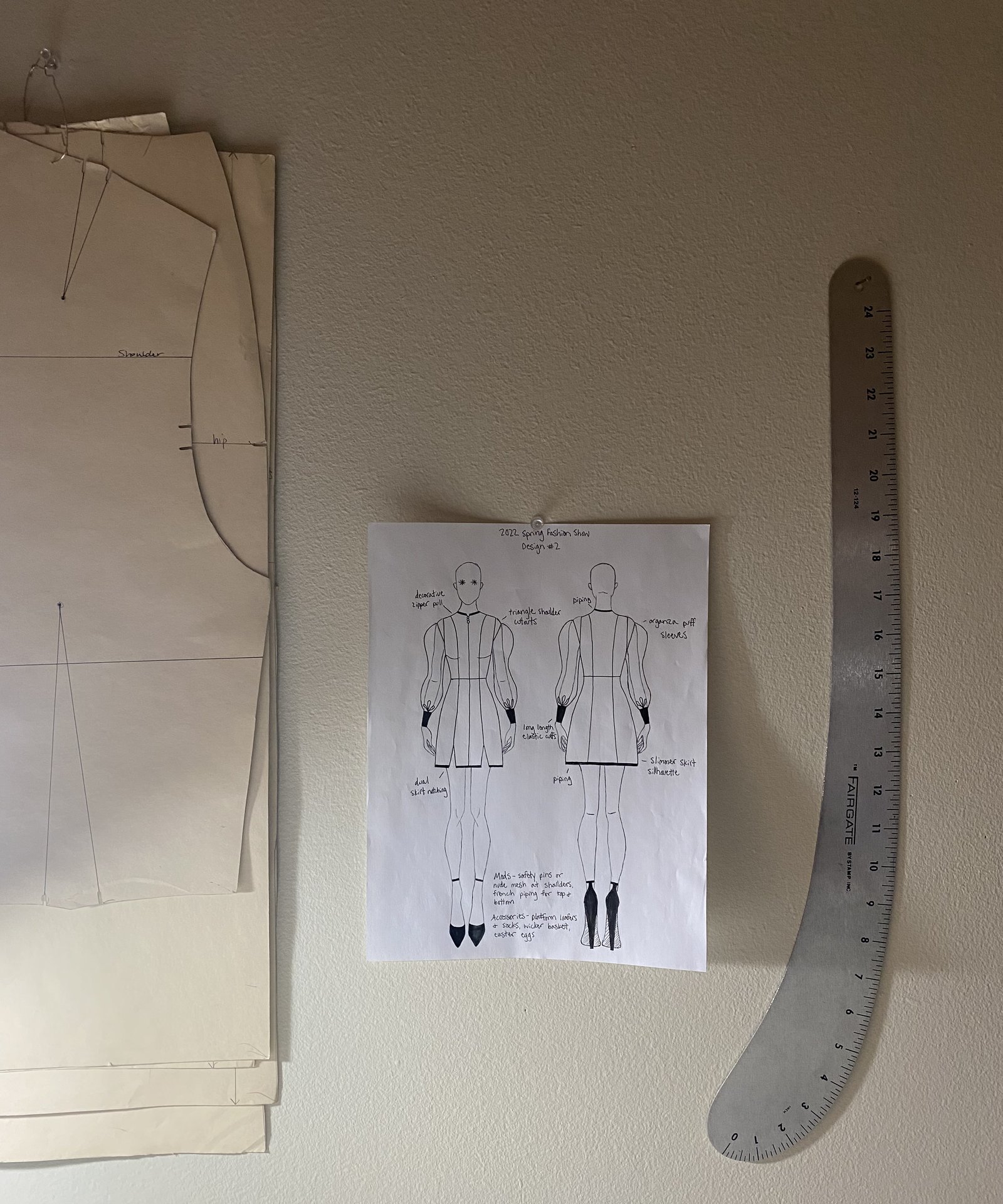 Drafted patterns and a fashion-show design sheet pinned to a studio wall
